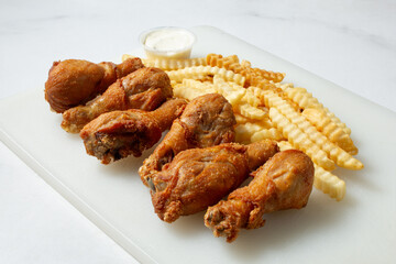A view of fried drumsticks and french fries, on a plastic cutting board.