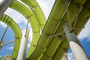 View from below of a green water slide structure in a modern aqua park, surrounded by lush greenery...