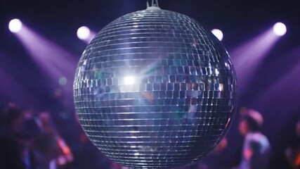 A mirrored disco ball hangs from the ceiling in a dark room lit by purple spotlights with blurred figures dancing below - Powered by Adobe