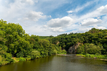 Fototapeta premium Serenity by the river in a lush green landscape with clouds drifting under a bright sky
