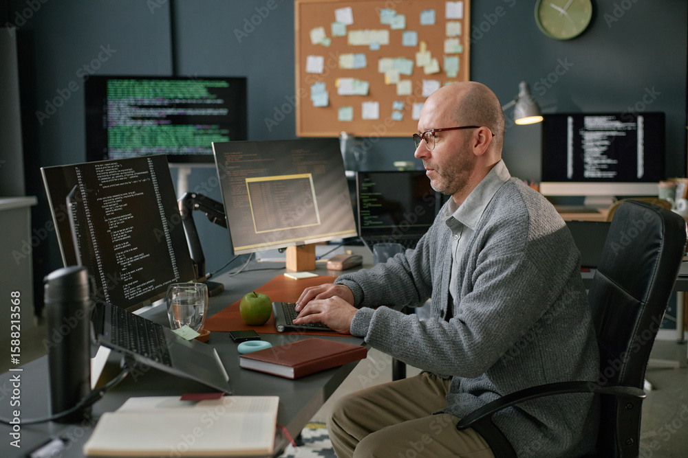 Poster middle aged caucasian man working at computer desk in modern office, typing on keyboard while analyz