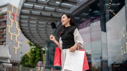 Asian woman female office worker walking outside shopping mall while holding red and white paper bag