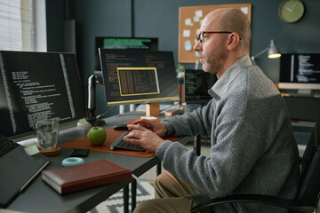 Middle aged Caucasian man working at computer desk, typing on keyboard and analyzing code on...