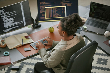 Young adult Black woman working at desk using desktop computer with code on monitors, typing on...