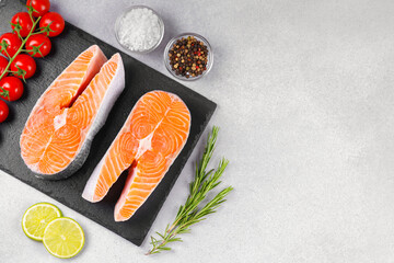Two fresh raw salmon steaks on white stone surface with food ingredients. Tomatoes, lime, rosemary,...