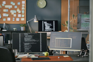 Modern office workspace featuring dual monitors displaying programming code, desktop computer,...