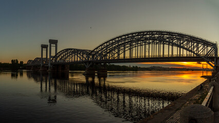 Silhouette of Finlyandsky Railway Bridge over Neva River at sunset with reflection in water and orange sky. Saint Petersburg, Russia.

