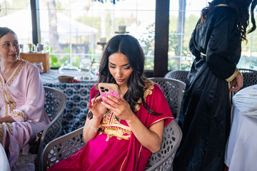 Arab woman distracted with phone at a festive gathering with friends in a decorated venue, while...