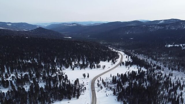 Aerial footage of a winding snow-covered road leading to Ust-Koksa in the Altai Republic, Russia. The video shows scenic winter landscapes with forests, hill
