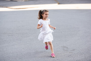 Happy child running in a white dress and pink sandals