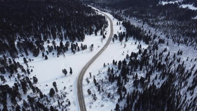 Aerial footage of a winding snow-covered road leading to Ust-Koksa in the Altai Republic, Russia. The video shows scenic winter landscapes with forests, hill