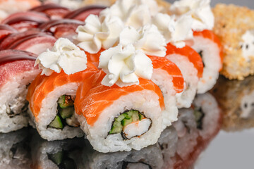 Freshly prepared sushi rolls topped with creamy dollops of cheese and filled with crab, cucumber, and rice sit beautifully arranged on a reflective black surface