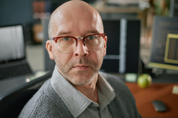 Portrait of middle aged Caucasian man with glasses looking into camera sitting at desk in modern...
