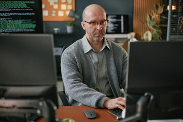 Portrait of middle aged Caucasian man wearing glasses sitting at desk working on computer monitors...