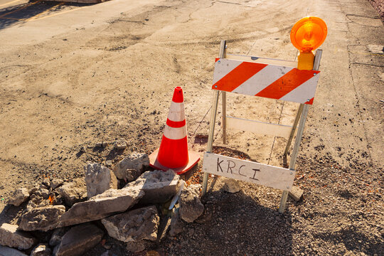 A traffic barrier and red and white cone and safety light on a road, roadworks by a pothole.