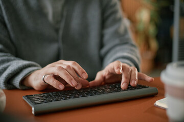 Caucasian middle aged man typing on wireless keyboard at desk, hands in focus with ring visible,...