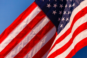 A large stars and stripes flag, the American flag fluttering in the breeze, in a blue sky.