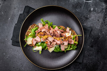 Toast with duck breast meat, foie gra, arugula and cheese on plate. black background. top view