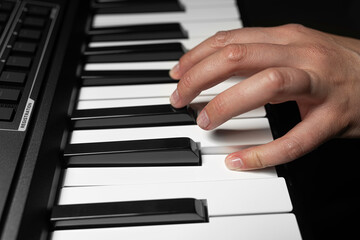 A pair of hands with long slender fingers gently presses down on the white keys of a digital piano...