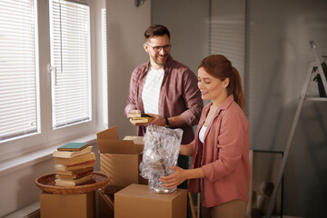 A couple is actively packing and moving into their new home, sorting through boxes filled with...