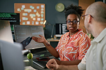 Young adult Black woman discussing project with Caucasian middle aged man in modern office, both...