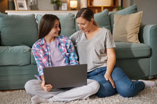 A mother and daughter sit comfortably on the floor of their living room, focused on a laptop, enjoying their time together and sharing a lighthearted moment. - Powered by Adobe
