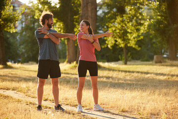 Two individuals perform dynamic stretching exercises in a sunlit park, promoting health and wellness through physical activity and engagement in nature.