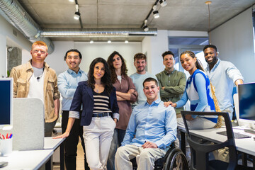 Diverse group of professionals standing together in a modern office, showcasing teamwork and inclusion with a colleague using a wheelchair