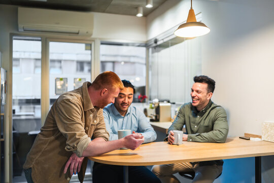 Businessmen enjoying a coffee break, talking and laughing together in a modern coworking space. One is chinese
