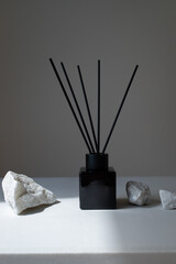 Aromatic bottle diffuser with sticks on modern minimalistic background decorated white stones for perfumed home.