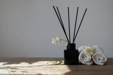 Modern composition of perfume in black glass diffuser with sticks decorated flowers and towels for home aromatherapy.