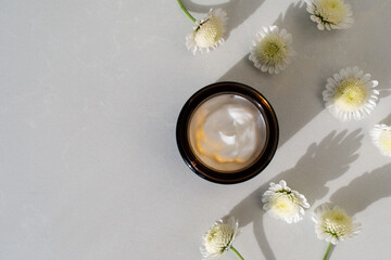 Jar of cosmetic cream on stone table decorated with flowers. Beauty, spa and skincare lifestyle aesthetic concept top view.