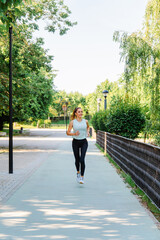 Mature female jogger running along tree-lined urban pathway, enjoying energetic fitness routine...