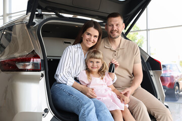 Happy family with keys sitting in car trunk in salon