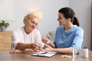 Fototapeta premium Nurse giving pills to senior woman at wooden table indoors. Home health care service
