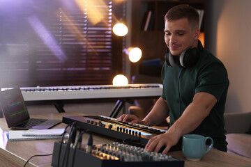 Man working with MIDI keyboard and dj mixer at table in home studio