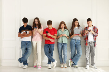 Obraz premium Teenagers with smartphones near white wall indoors