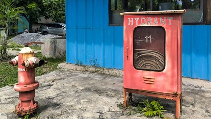 Vintage fire protection equipment including a hydrant and hose cabinet number 11 on a cracked concrete base.