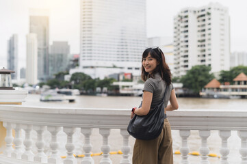 Fototapeta premium Happy solo southeast asian woman teenager blogger. World travel and asia tourism concept. Local cultural experience for explorer to wait for express boat on Chao Phraya River Bangkok Thailand
