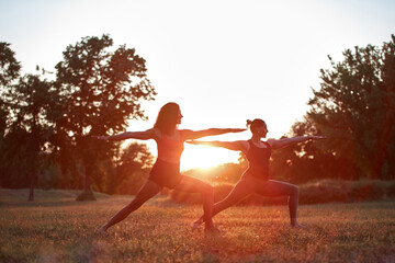 Two women practicing yoga and stretching in the park on a hot sunny summertime day.