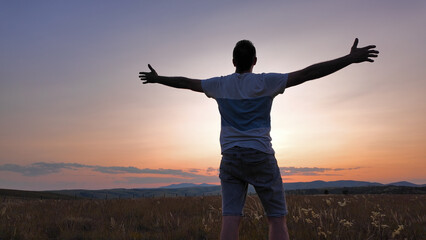 Silhouette of a man with arms wide open in nature.
