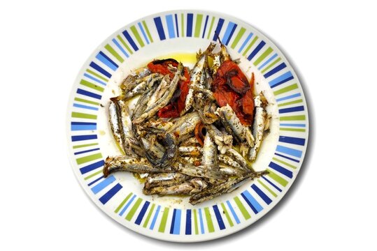 Top view of a plate of fried anchovies (gavros tiganitos) drizzled with virgin olive oil, paired with fried tomatoes, and finished with a sprinkle of aromatic oregano, a classic Greek seafood delight.