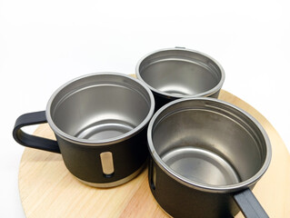 Three black stainless steel mugs arranged on a round wooden board, isolated on white background....