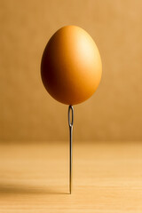 Conceptual image of a brown egg perfectly balanced on the eye of a needle on wooden surface