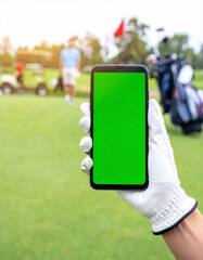 A golfer's gloved hand holding a smartphone with a green screen mockup on a morning golf course with caddy, golf cart, bag, and hole in background.