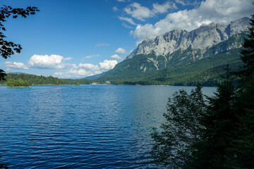 Obraz premium Summer view of the Zugspitze massif behind Eibsee lake with blue sky and lush forest in Germany