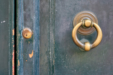 Close-up of an old, weathered green wooden door featuring a brass knocker and keyhole, highlighting...
