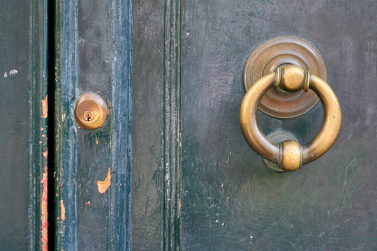 Close-up of an old, weathered green wooden door featuring a brass knocker and keyhole, highlighting its age and history.
