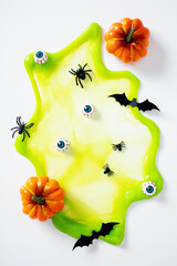 Halloween flat lay with green slime, spiders, bats, eyeballs, and small pumpkins on white background