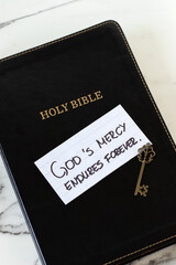 God's mercy endures forever handwritten quote on top of holy bible book with ancient key. Christian biblical concept.